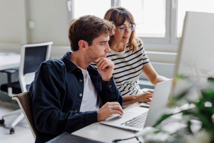 Two focused colleagues collaborating on a project using a laptop in a modern office